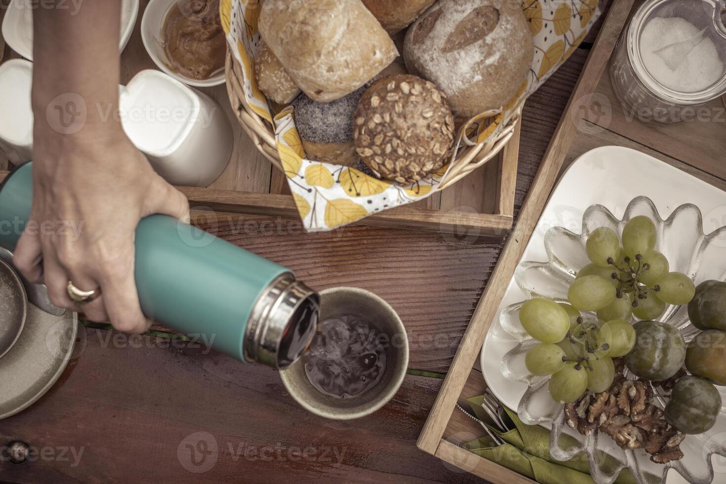 Overhead shot of wooden breakfast table with bread, fruits, and pouring in coffee photo