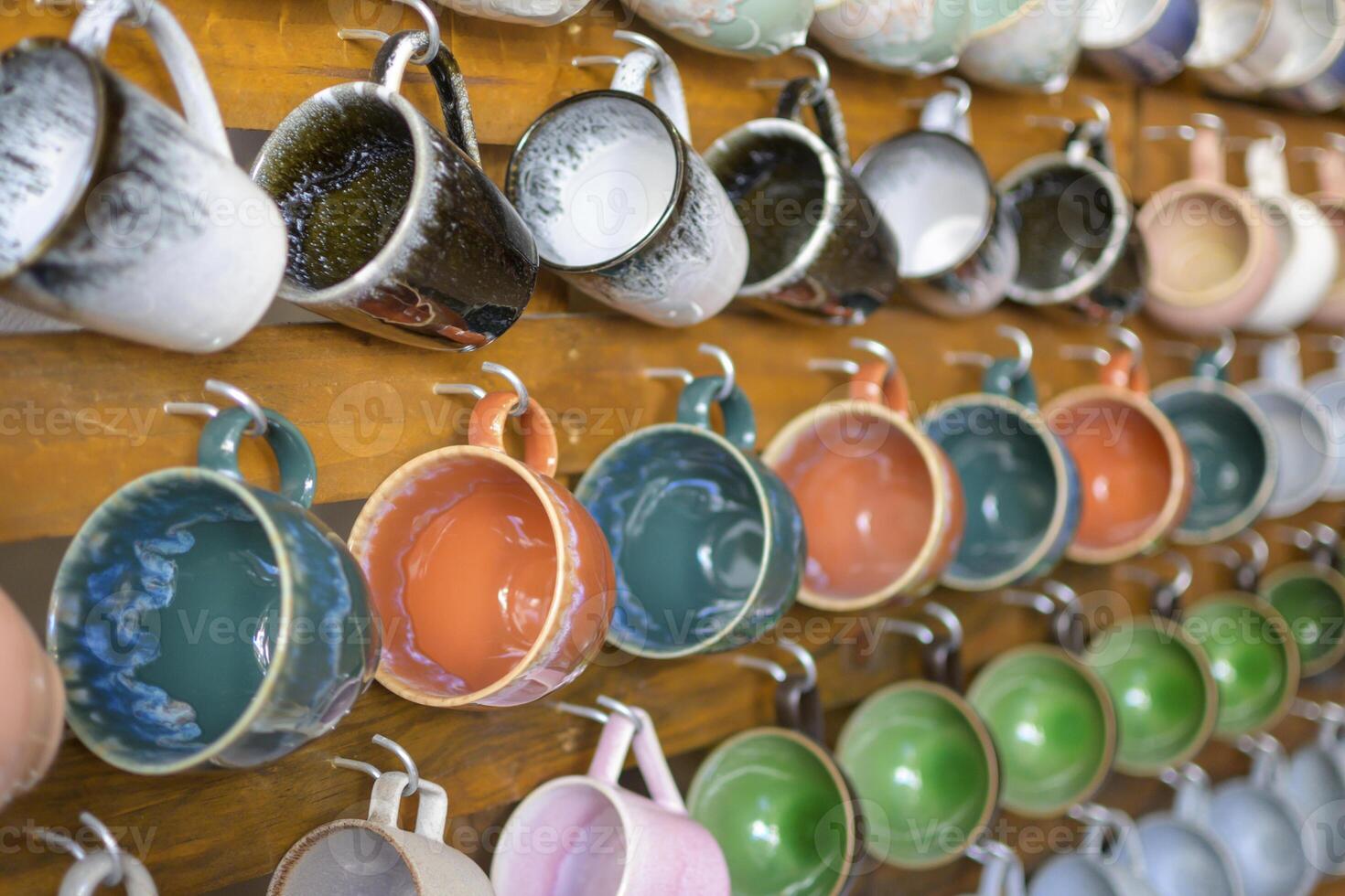 Collection of colorful ceramic mugs hanging on a wooden wall photo