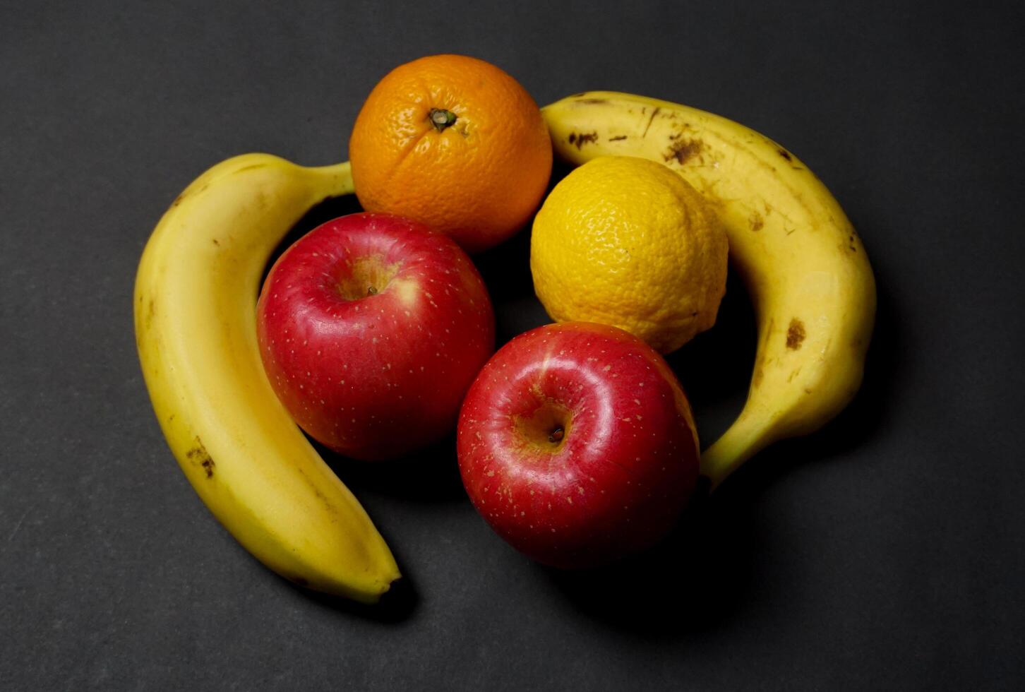 Bananas, apples, lemons and oranges on a black background. photo