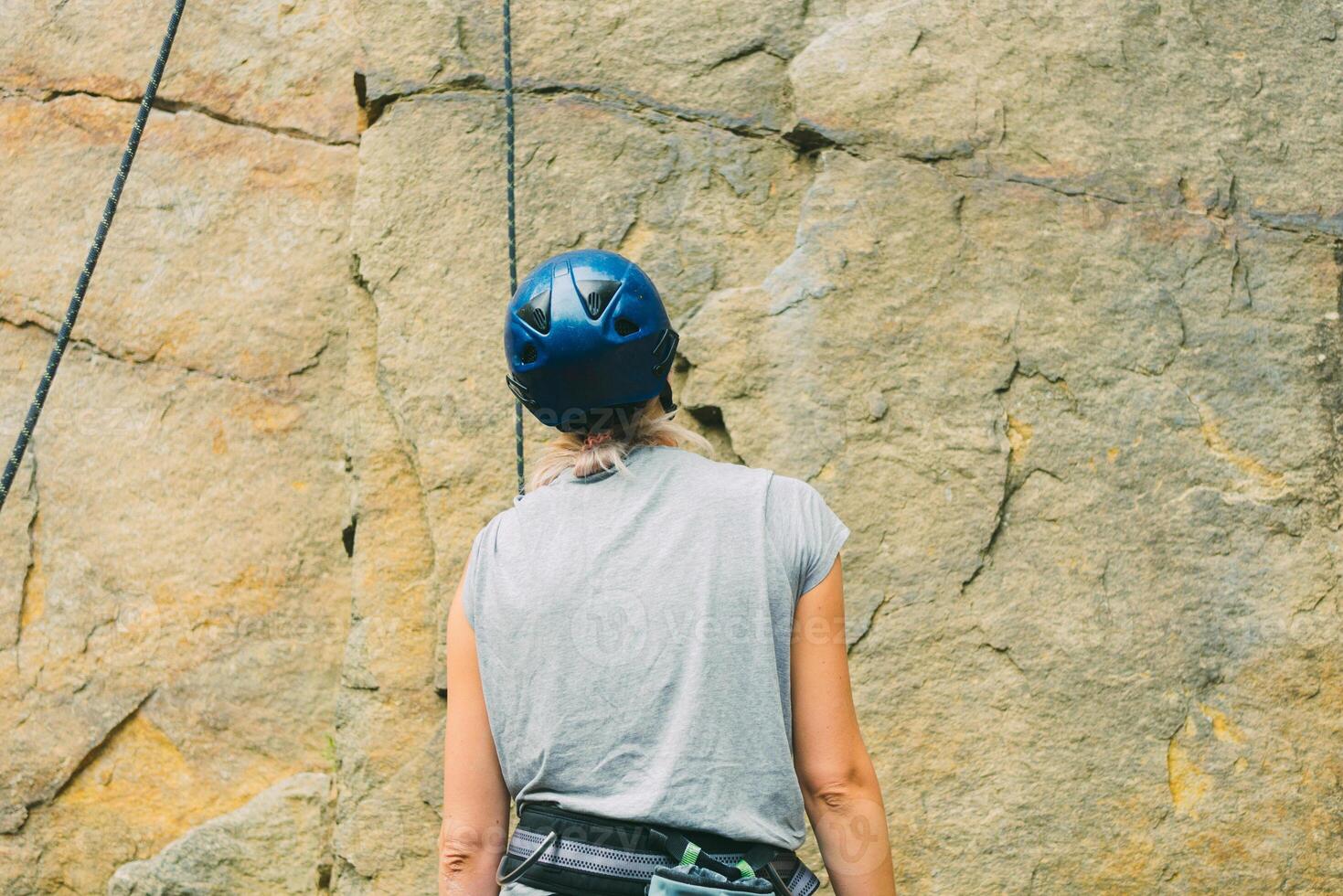 joven atlético mujer en equipo en pie en frente de Roca rock al aire libre y consiguiendo Listo a trepar. formación zona para al aire libre actividades. extremo deporte. posterior ver foto