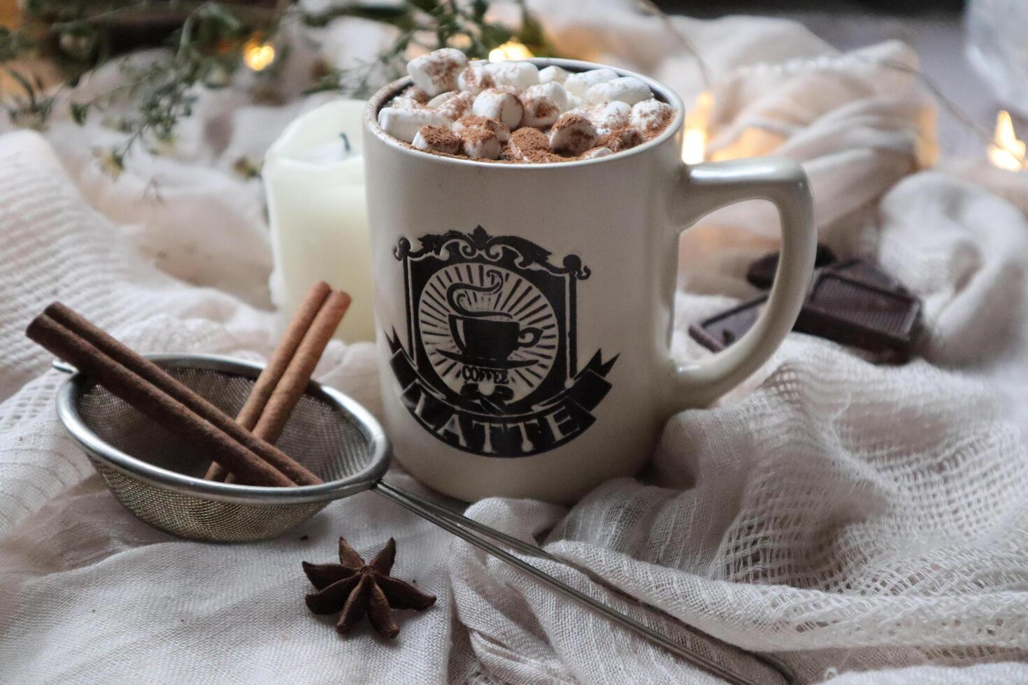 Hot cocoa with marshmallow in a white ceramic mug surrounded by drink preparation ingredients. Cosy winter composition photo