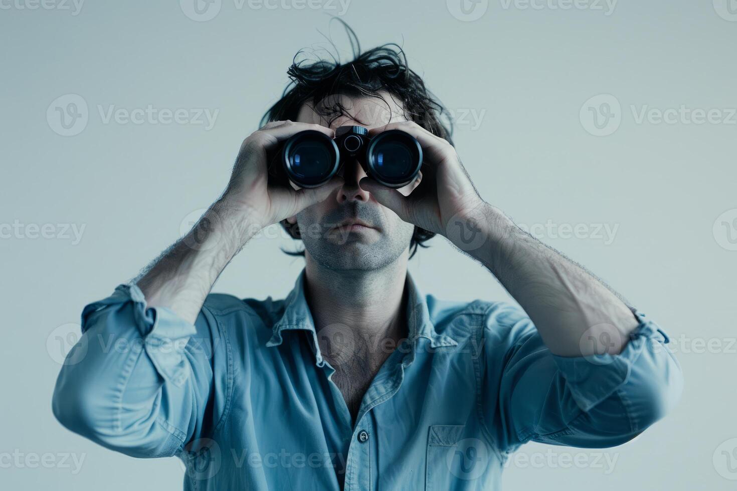 Young man looking through binoculars, serious expression photo