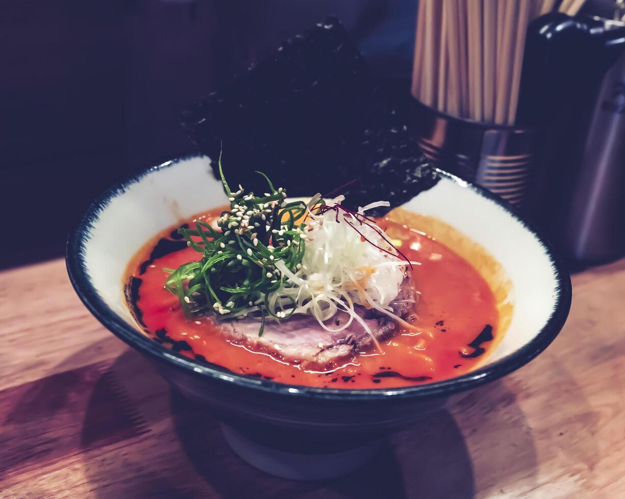 Ramen, a dish with orange broth consisting of pork, vermicelli, half boiled egg, dried seaweed and topped with chopped spring onions and white sesame seeds. photo