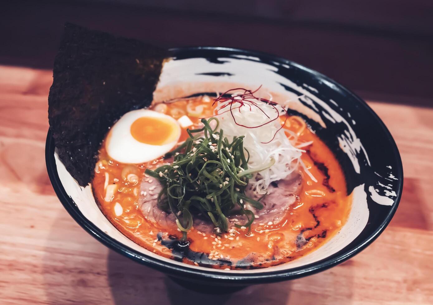 Ramen, a dish with orange broth consisting of pork, vermicelli, half boiled egg, dried seaweed and topped with chopped spring onions and white sesame seeds. photo