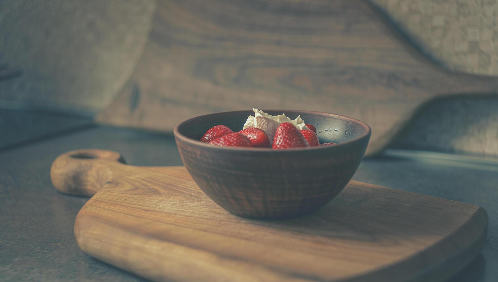 Home kitchen. Juicy strawberries with cream in a clay plate on a wooden board photo