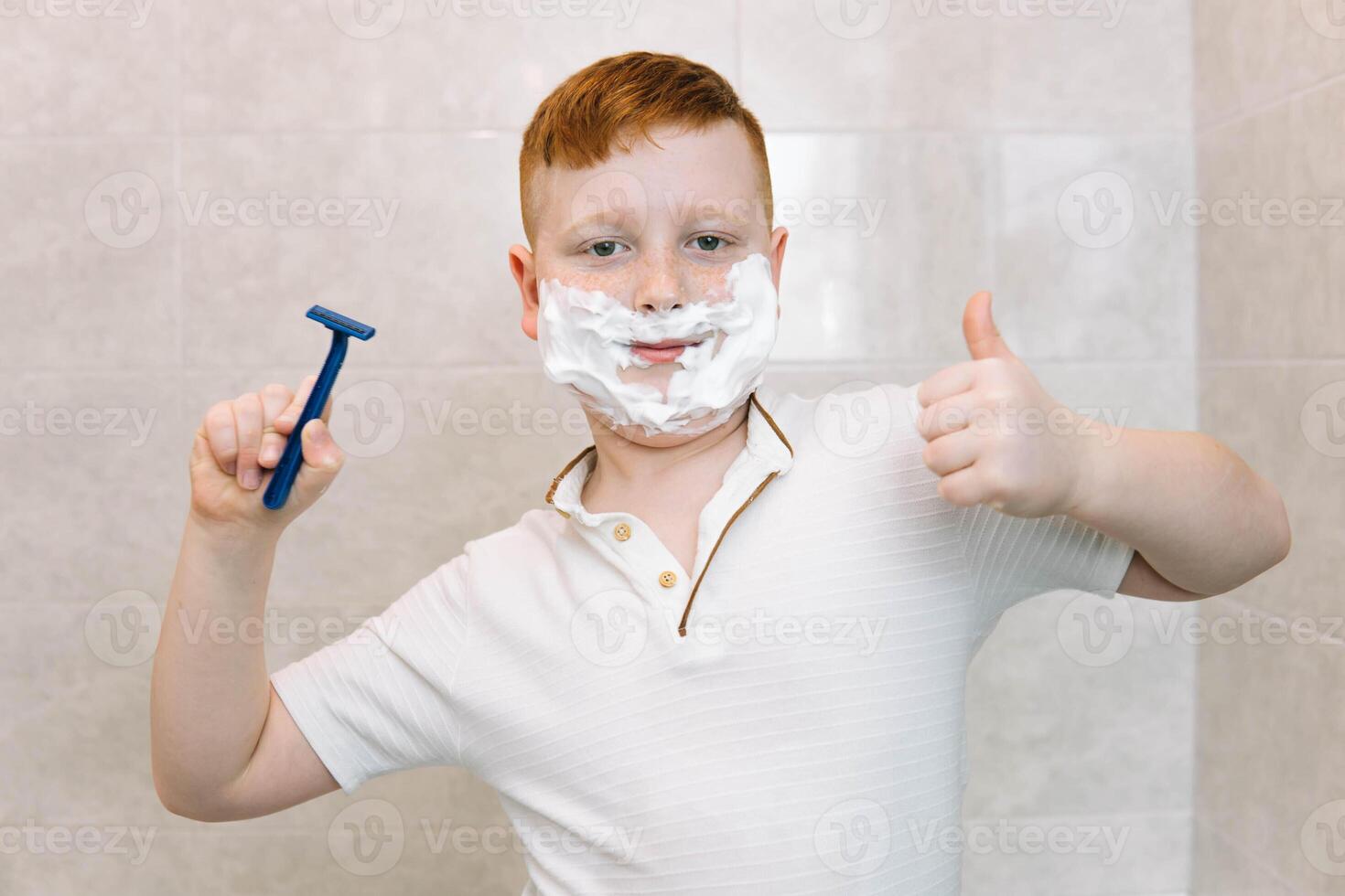 gracioso chico en el bañera con afeitado crema en su cara y afeitado maquinilla de afeitar foto