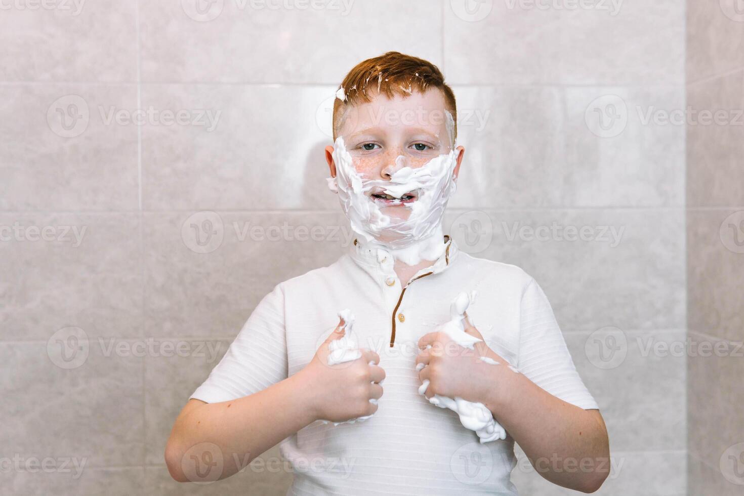 gracioso chico en el bañera con afeitado crema en su cara muestra un firmar de consentimiento con su pulgar arriba foto