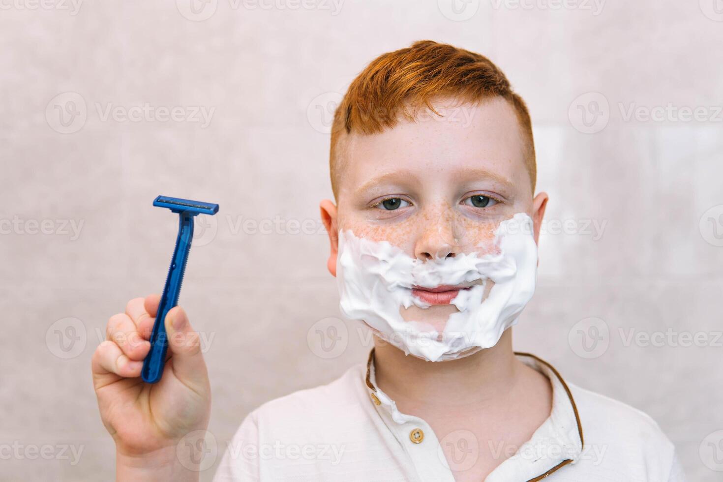 Funny boy in the bath with shaving cream on his face and shaving razor photo