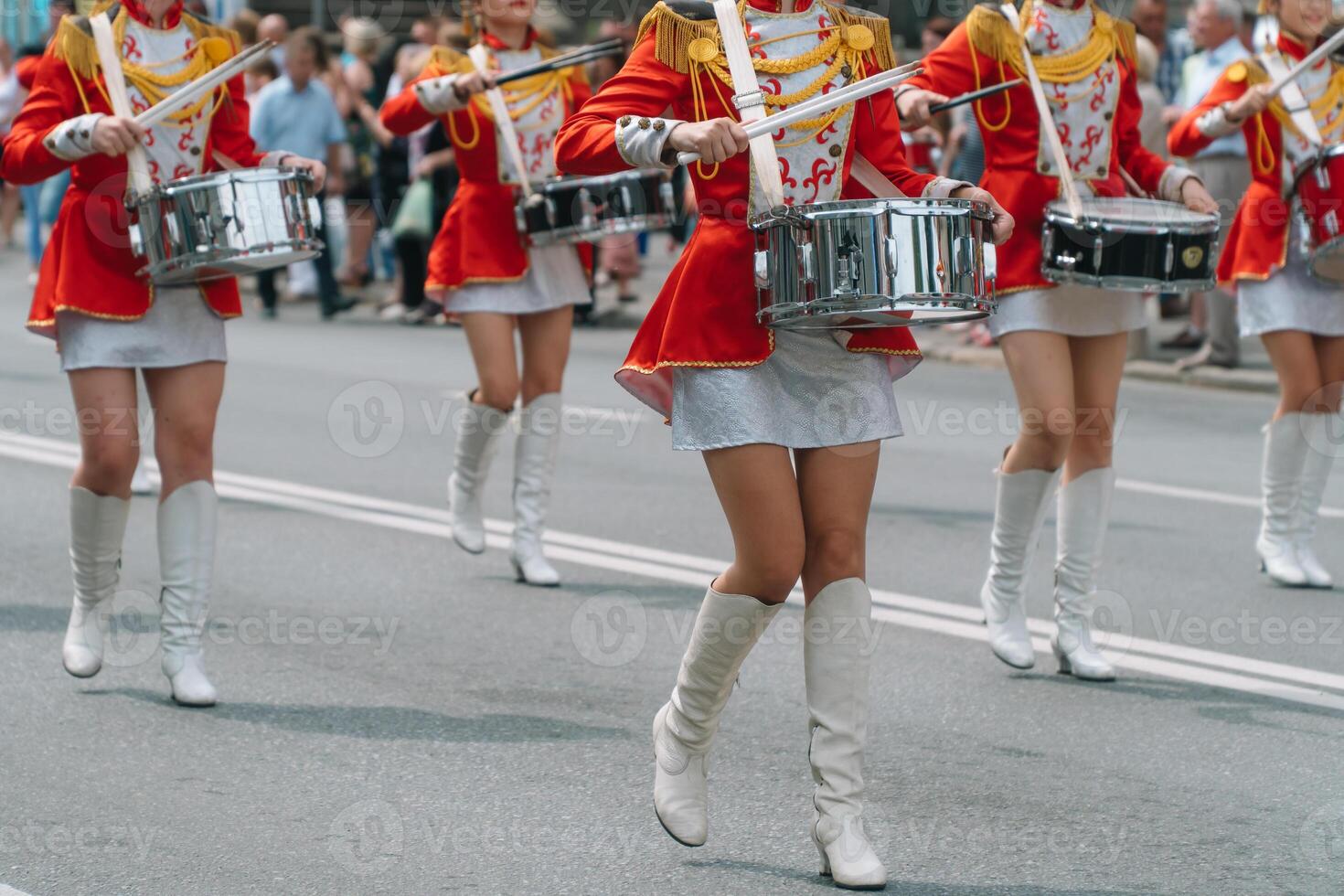 Street performance of festive march of drummers girls in red costumes on city street. Young girls drummer in red vintage uniform at the parade photo
