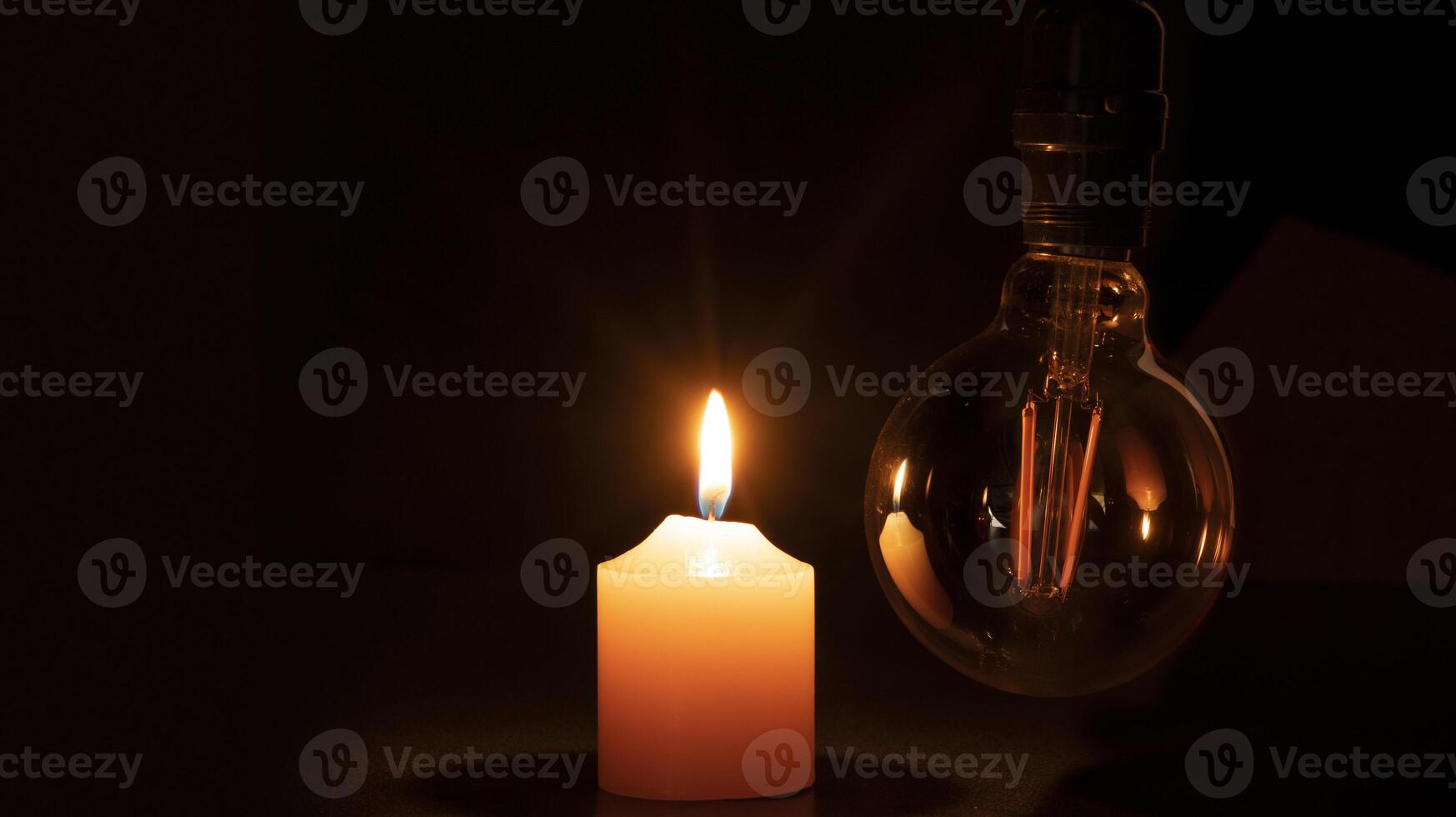 Blackout concept, turned off light bulb with no electricity hanging next to a burning candle photo