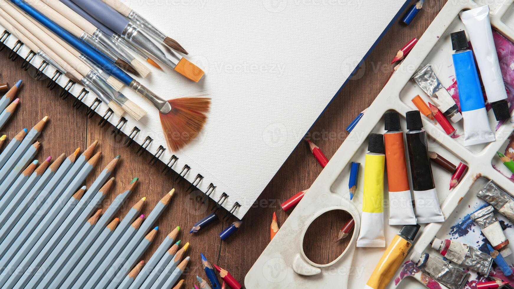 Top view of wooden table with pencils, paint tubes, art supplies, variety of brushes photo