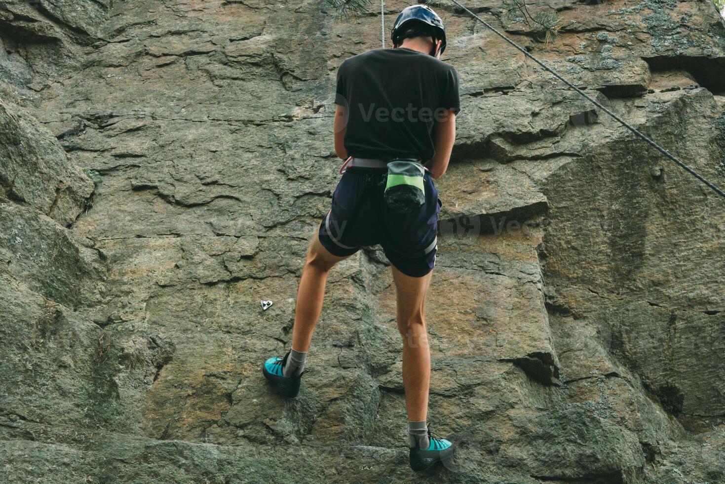 Young man in equipment doing rock climbing outdoors. Training area for outdoor activities. Extreme sport. photo