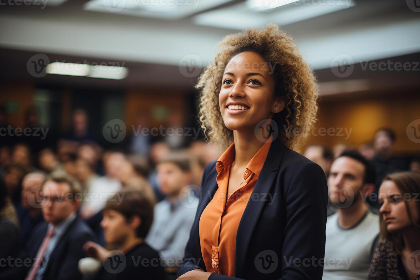 A woman standing confidently in front of a large crowd of people, who are listening attentively. photo