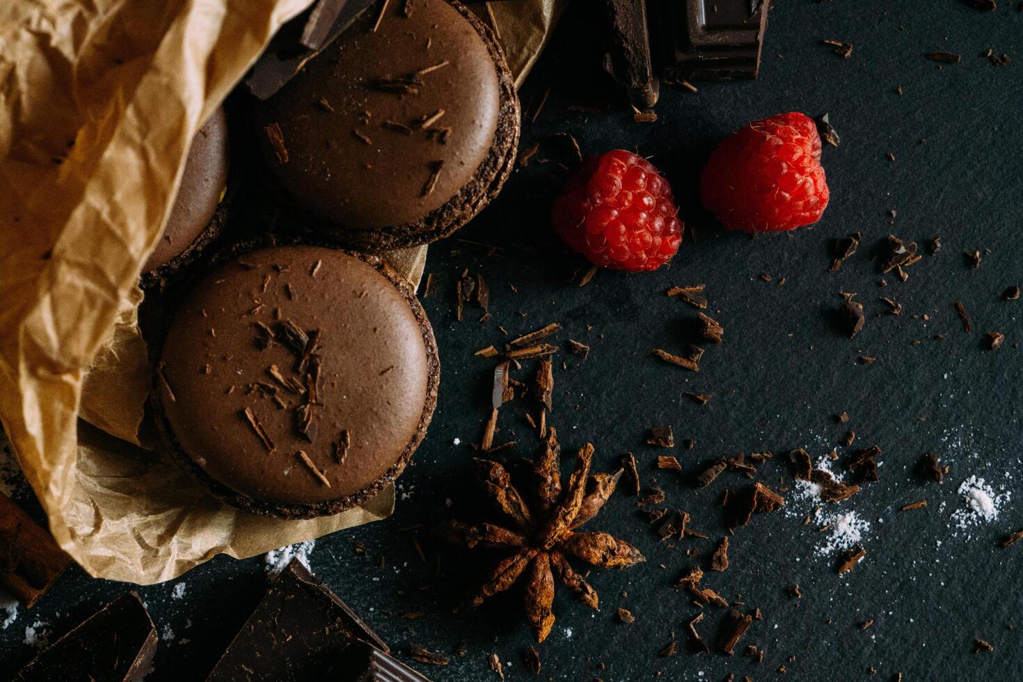 chocolate macarons con frambuesas en un oscuro antecedentes foto