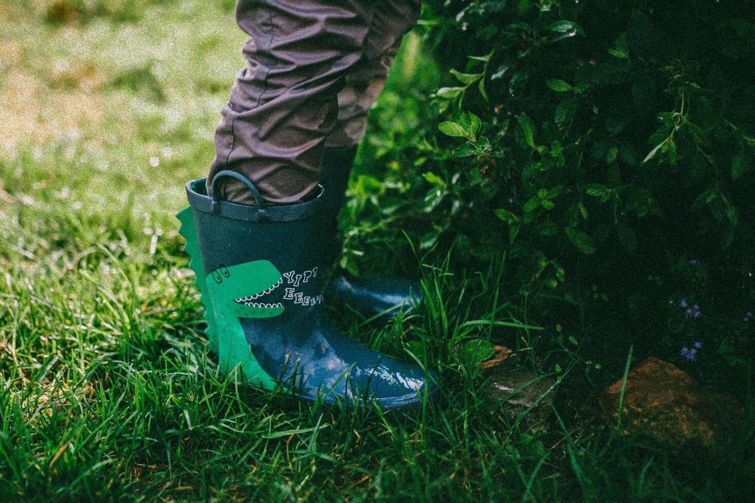 a person wearing green rain boots standing in the grass photo