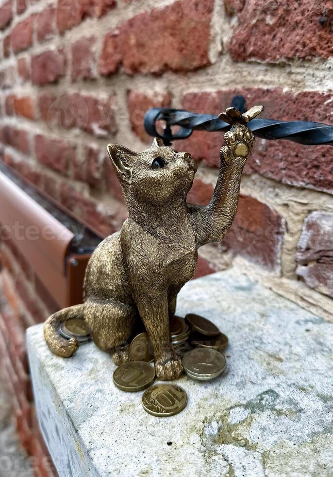 An artistic bronze cat figurine holding a pair of eyeglasses, surrounded by scattered coins on a stone ledge. photo
