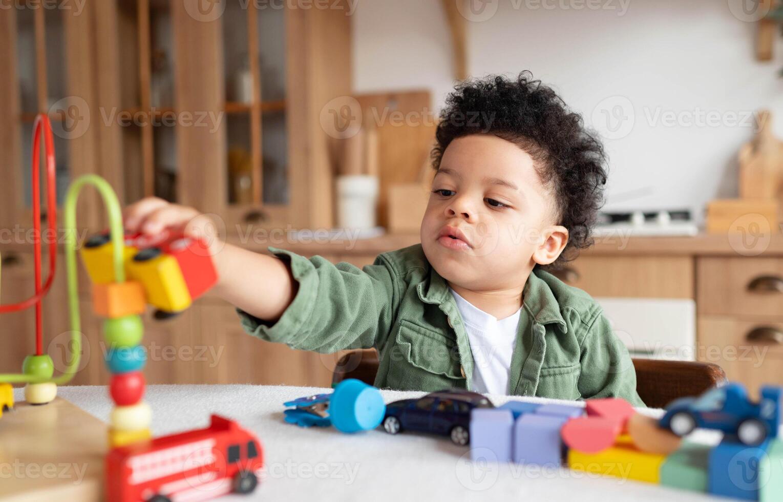 Concentrated little african american boy with bushy curly hair playing with colorful wooden blocks, enjoying table games playing alone at home kitchen , close up photo