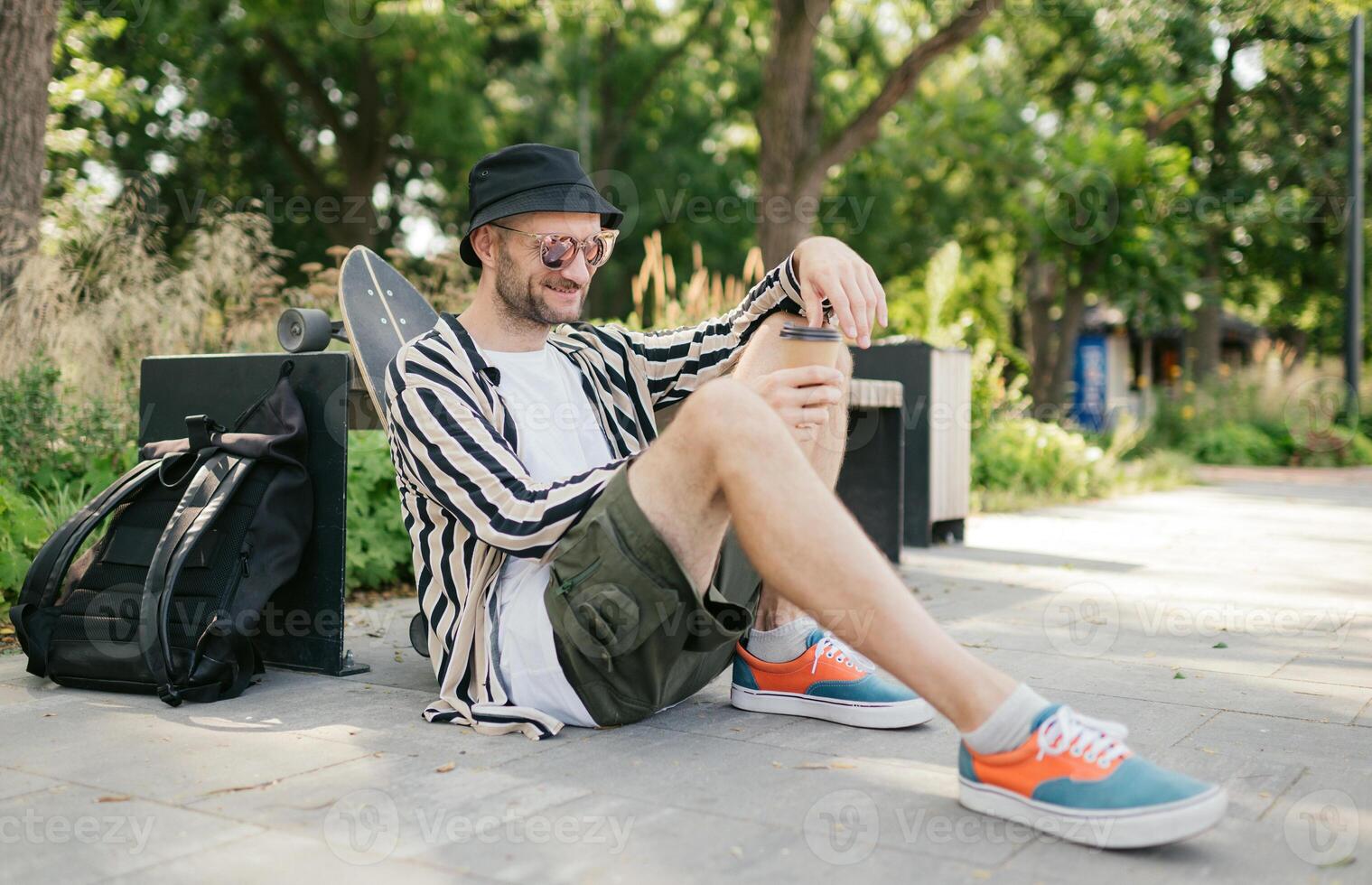 Portrait of smiling adult male who drinking coffee at extreme park near skateboard, summer vibe. resting photo