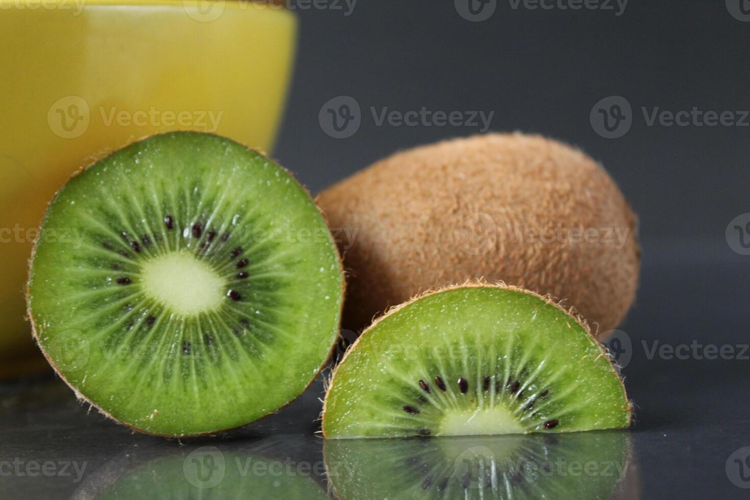 still life of kiwi fruit in a yellow bowl plate and pieces of mug next to on a black background with a reflection of there is a copyspace photo