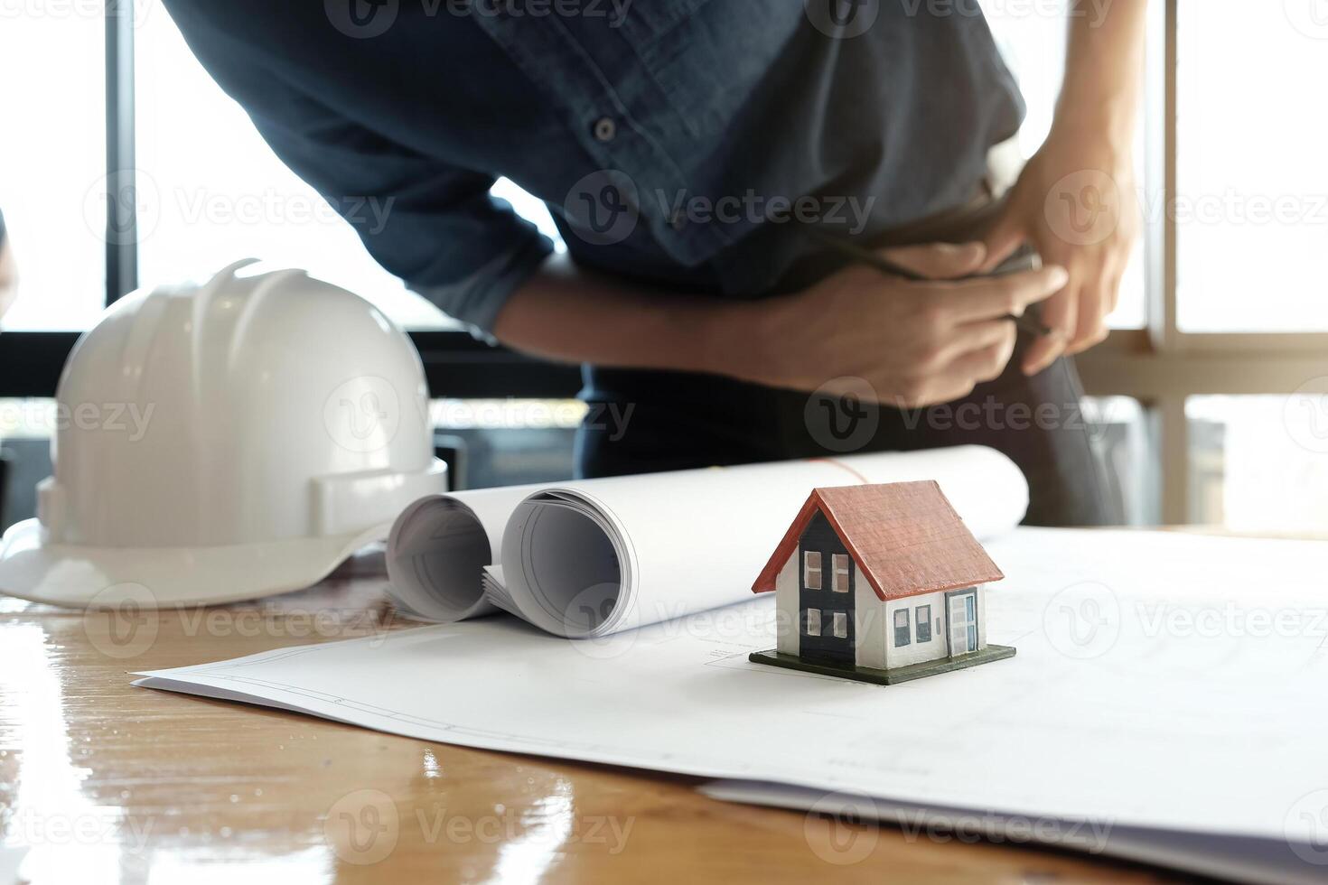 Engineer sketching a building project design with mockup house model and blueprints. Architect man working with compasses and blueprints for architectural plan. photo