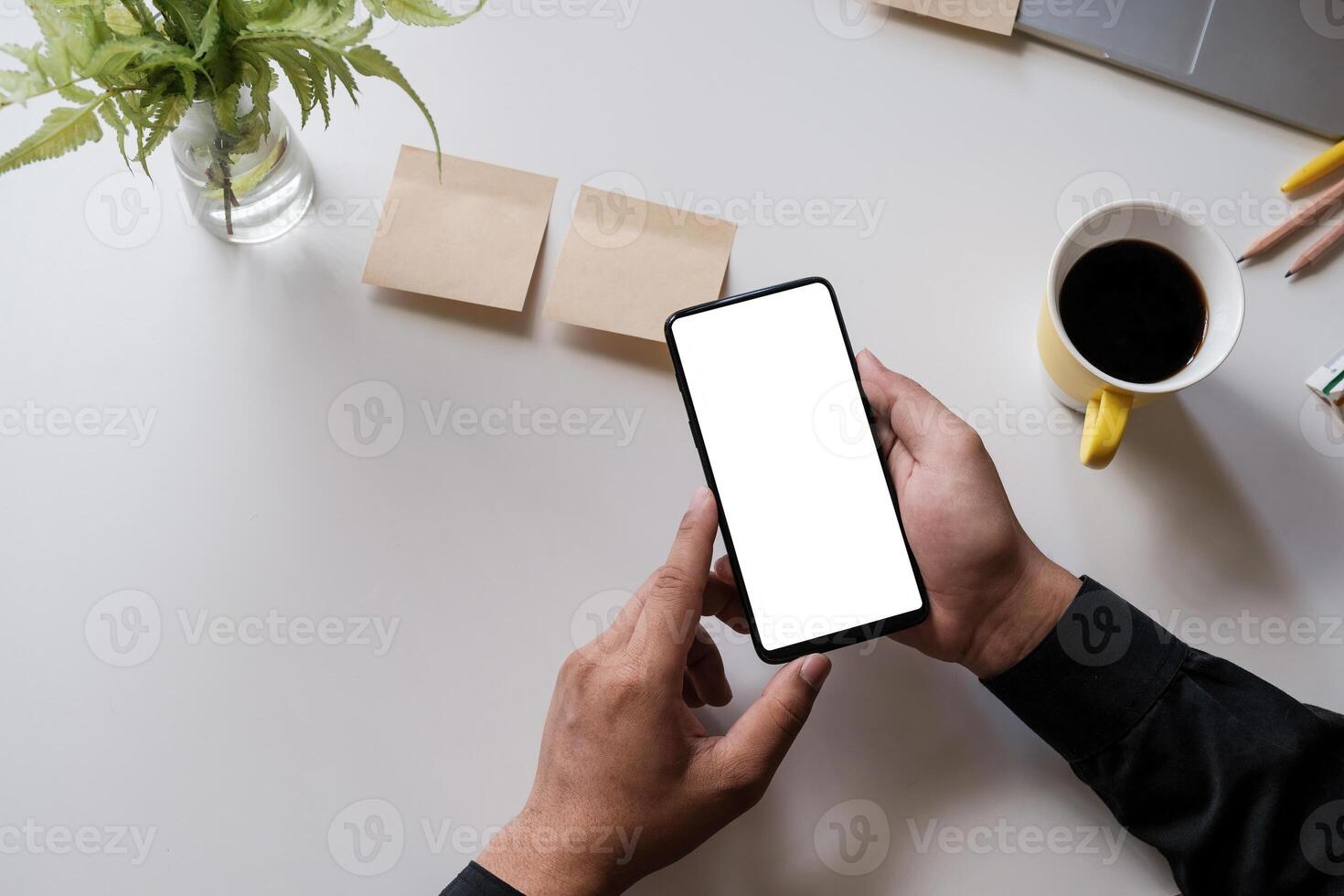 Close up of a man holding smartphone with blank screen mobile on wooden desk in home office, top view photo