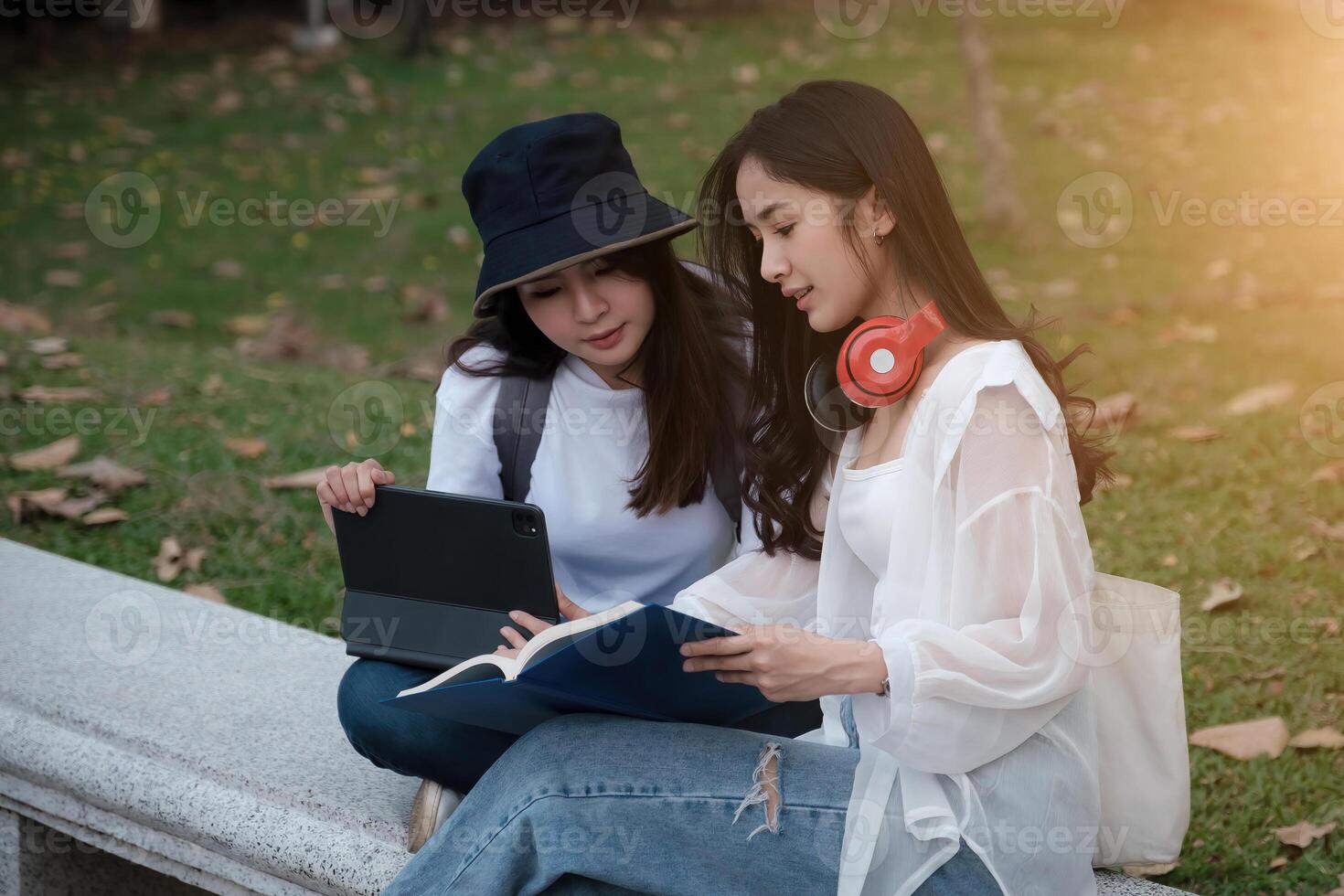 Two students are sitting in park during reading a book and communication. Study, education, university, college, graduate concept. photo