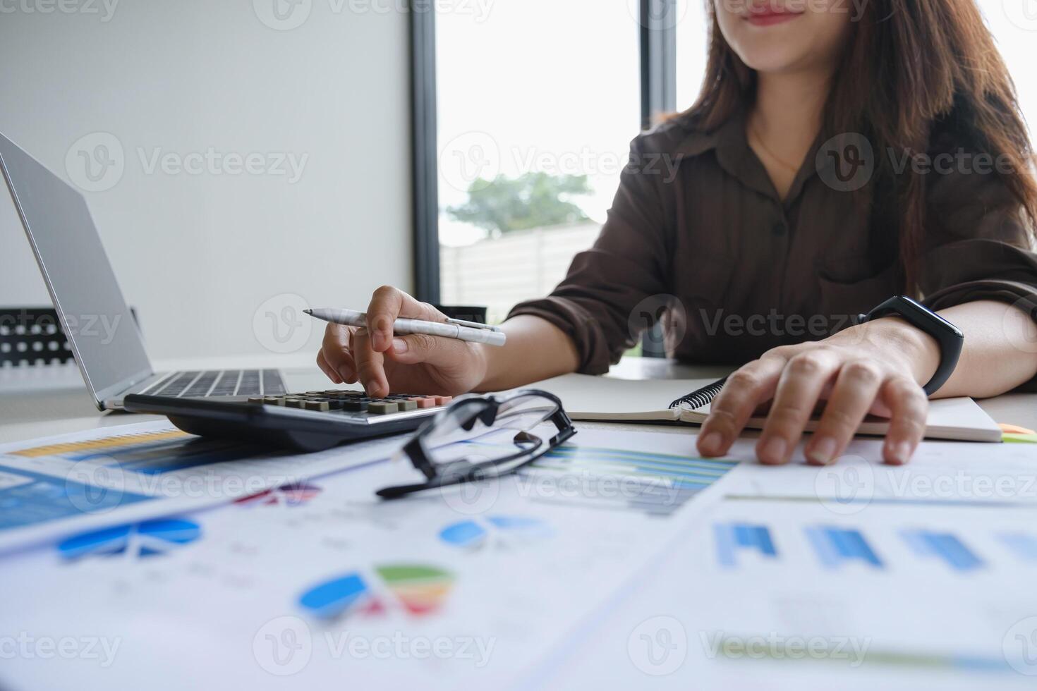 Close up Hand of Businesswoman pointing and analyzing charts by document and laptop computer. photo