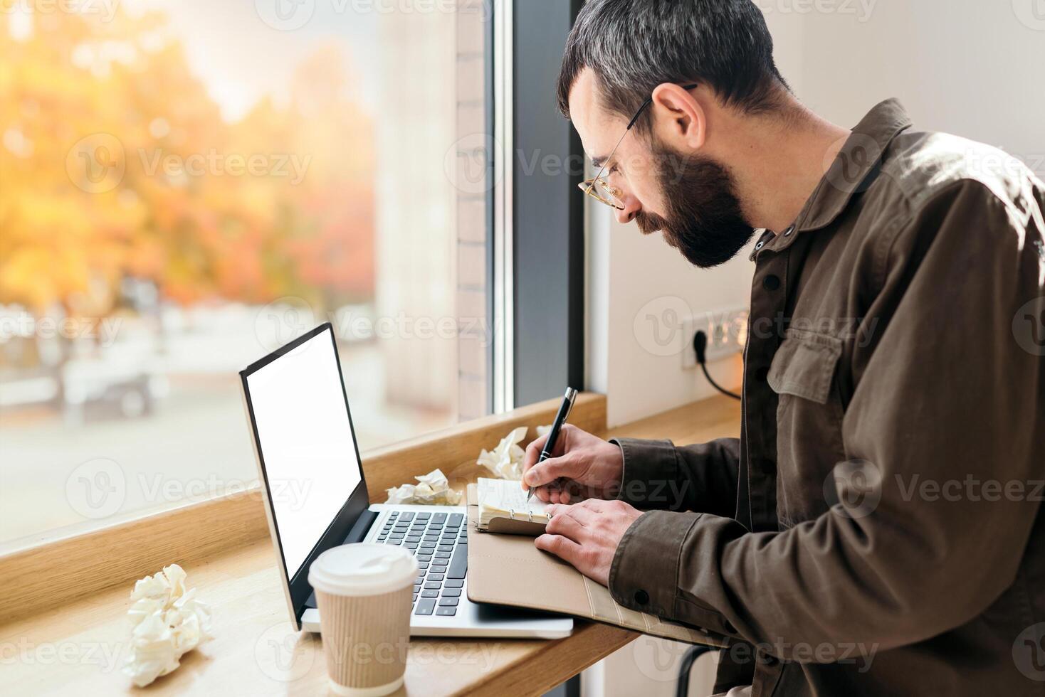 Bearded business man in casual style writing in a notebook in a cafe. work process, A man sits in a cafe with a laptop, remote work, freelance, autumn photo