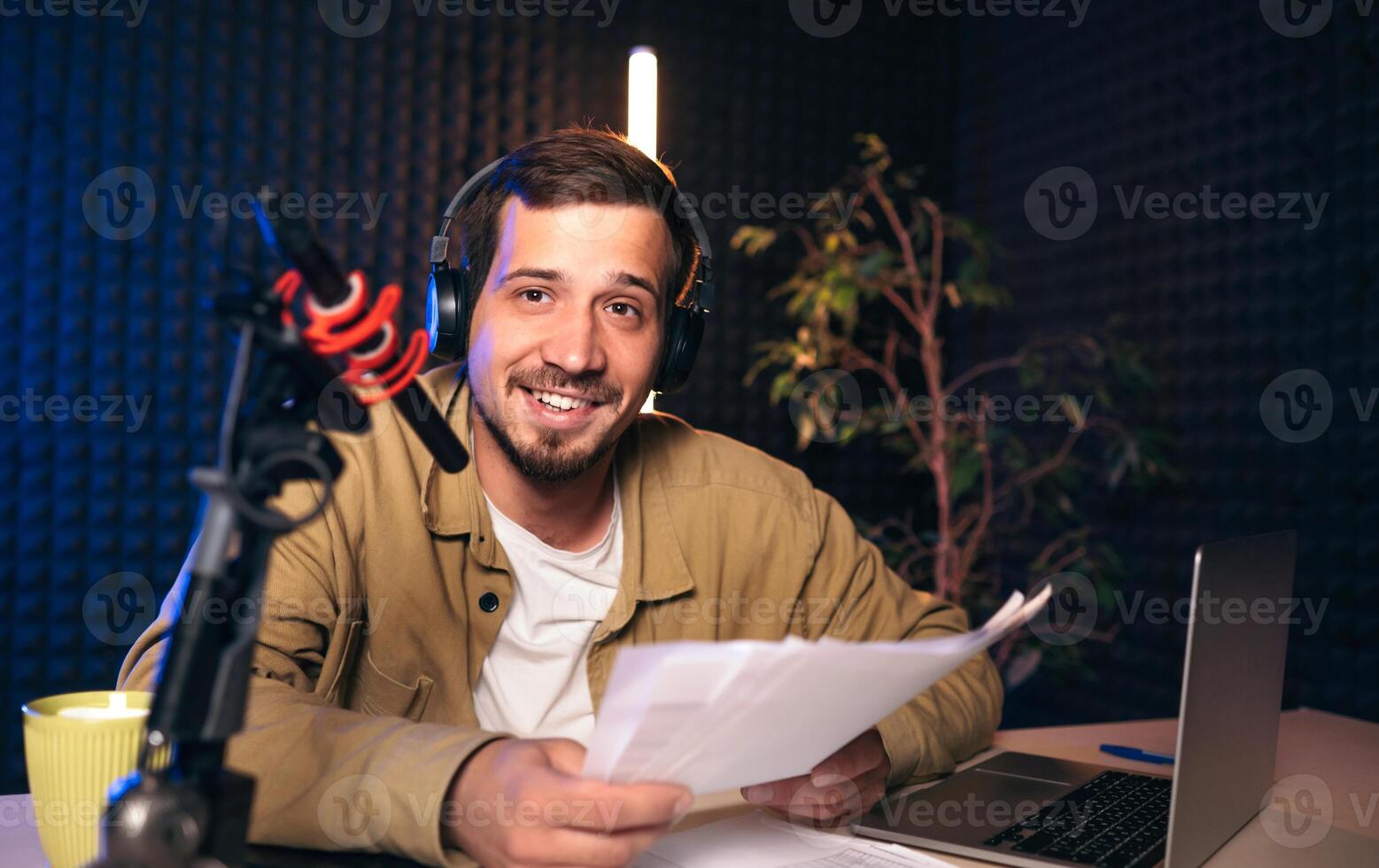 sonriente radio anfitrión con auriculares leyendo Noticias desde papel dentro estudio micrófono a radio estación con neón luces. mirando a cámara foto