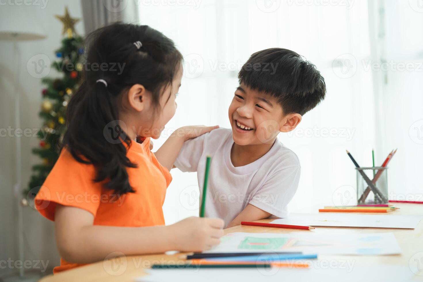Two children are sitting at a table with crayons and coloring books. They are smiling and laughing, enjoying their time together. Concept of happiness and friendship between the two children photo