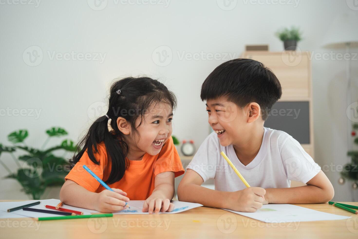 Two children are sitting at a table with crayons and drawing paper. They are smiling and laughing, enjoying their time together. Concept of happiness and playfulness photo