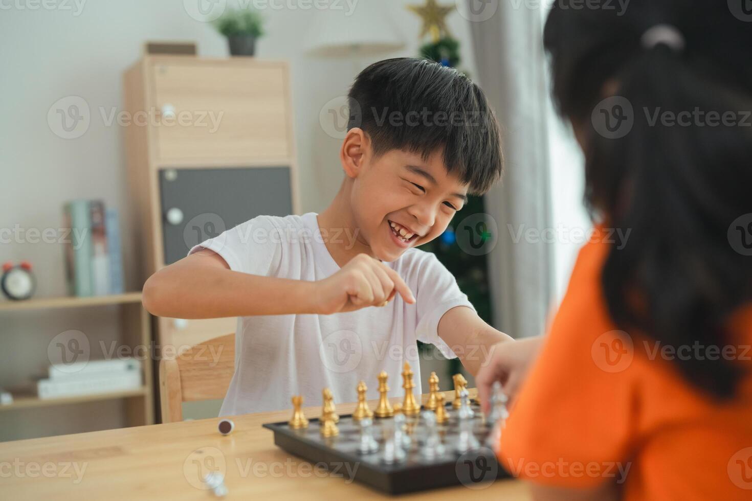 Two children playing a game of chess. One is smiling and the other is frowning. The boy in the white shirt is smiling and the girl in the orange shirt is frowning photo