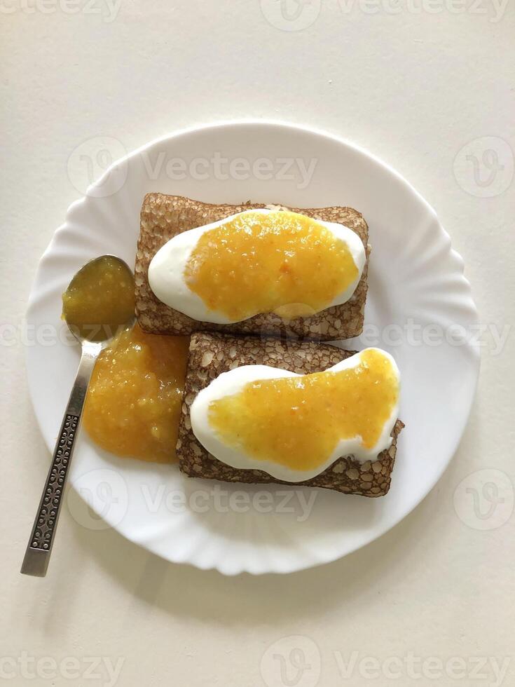 two delicious pancakes with sour cream and orange jam on a plate, view from above photo