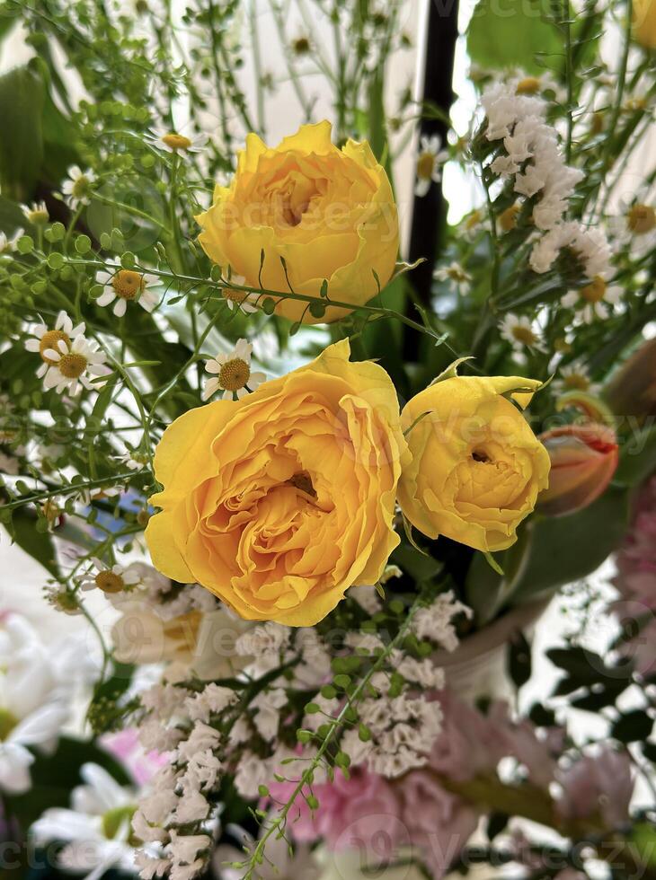 Close-up of a fresh bouquet featuring bright yellow roses among delicate white flowers and green foliage, perfect for vibrant spring and summer themes. photo