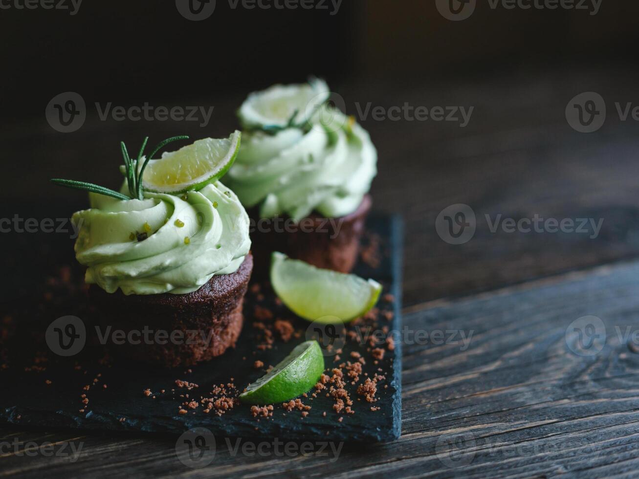 Tasty chocolate cupcake with buttercream icing and lime slices on a wooden table. photo
