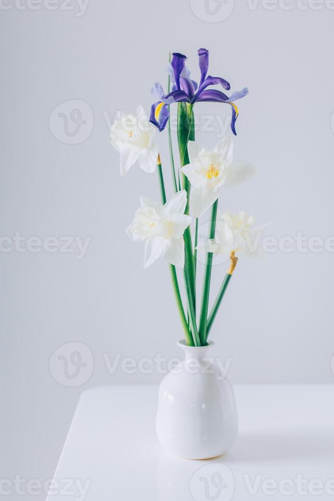 Bouquet of tender Daffodil narcissus and Iris flowers in a vase on a white table. photo