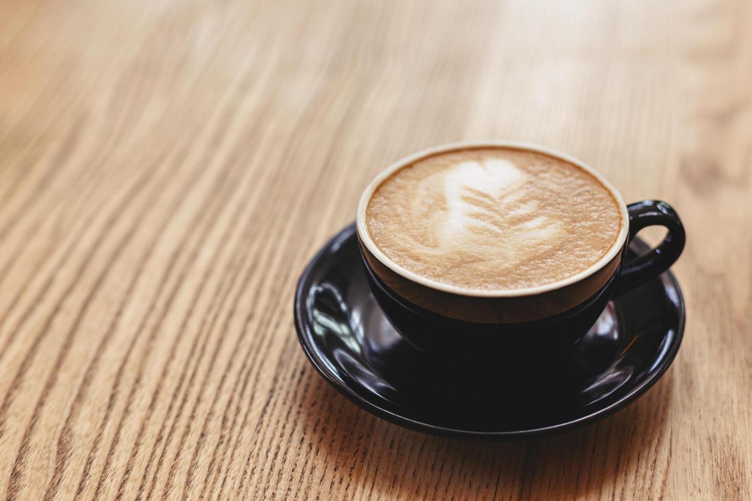 taza de capuchino con latté Arte en de madera antecedentes. negro cerámico taza, sitio para texto. foto