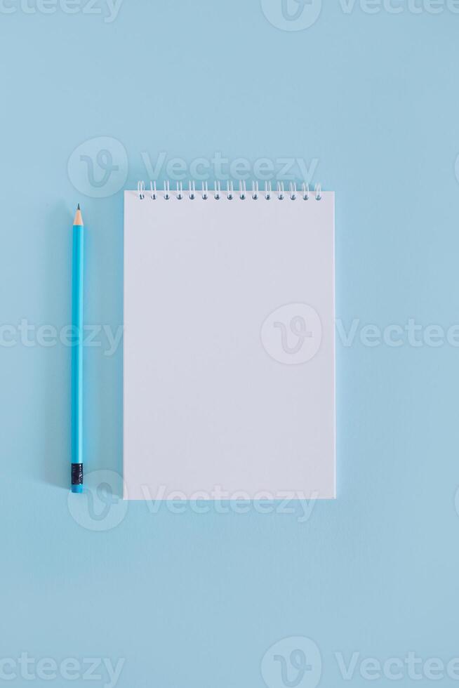 Notebook with blank page and pencil on light blue background. photo