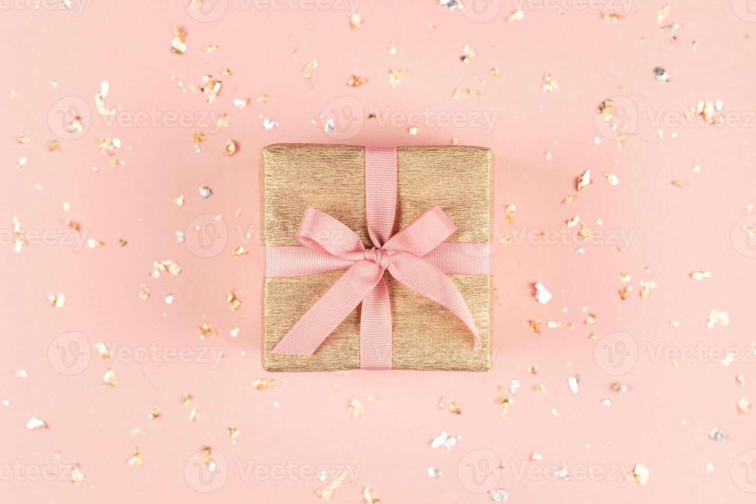 Golden gift box with pink bow on the pink background with golden and silver sparkles. photo