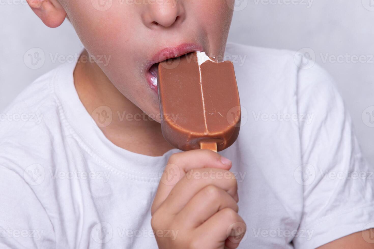 A boy whose face is unrecognizable eats ice cream covered in chocolate. photo