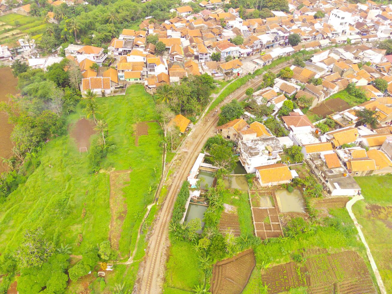 Bird's eye view from drone of a railroad track between residential areas and rice fields in Cicalengka, Indonesia. Shot from a drone flying 200 meters high photo
