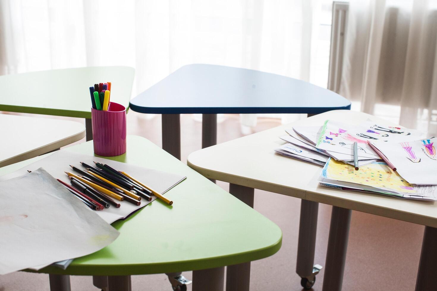 A group of multi-colored, triangular study tables with a box of colored pencils and papers with drawings on top of them photo