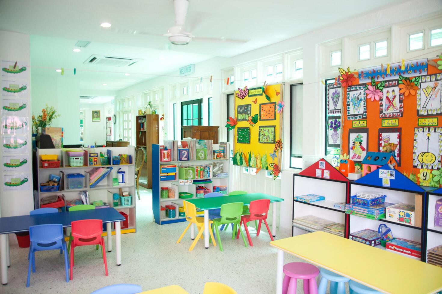 interior of a classroom with colorful tables and chairs with a wall hanging above it, a school storage cabinet photo