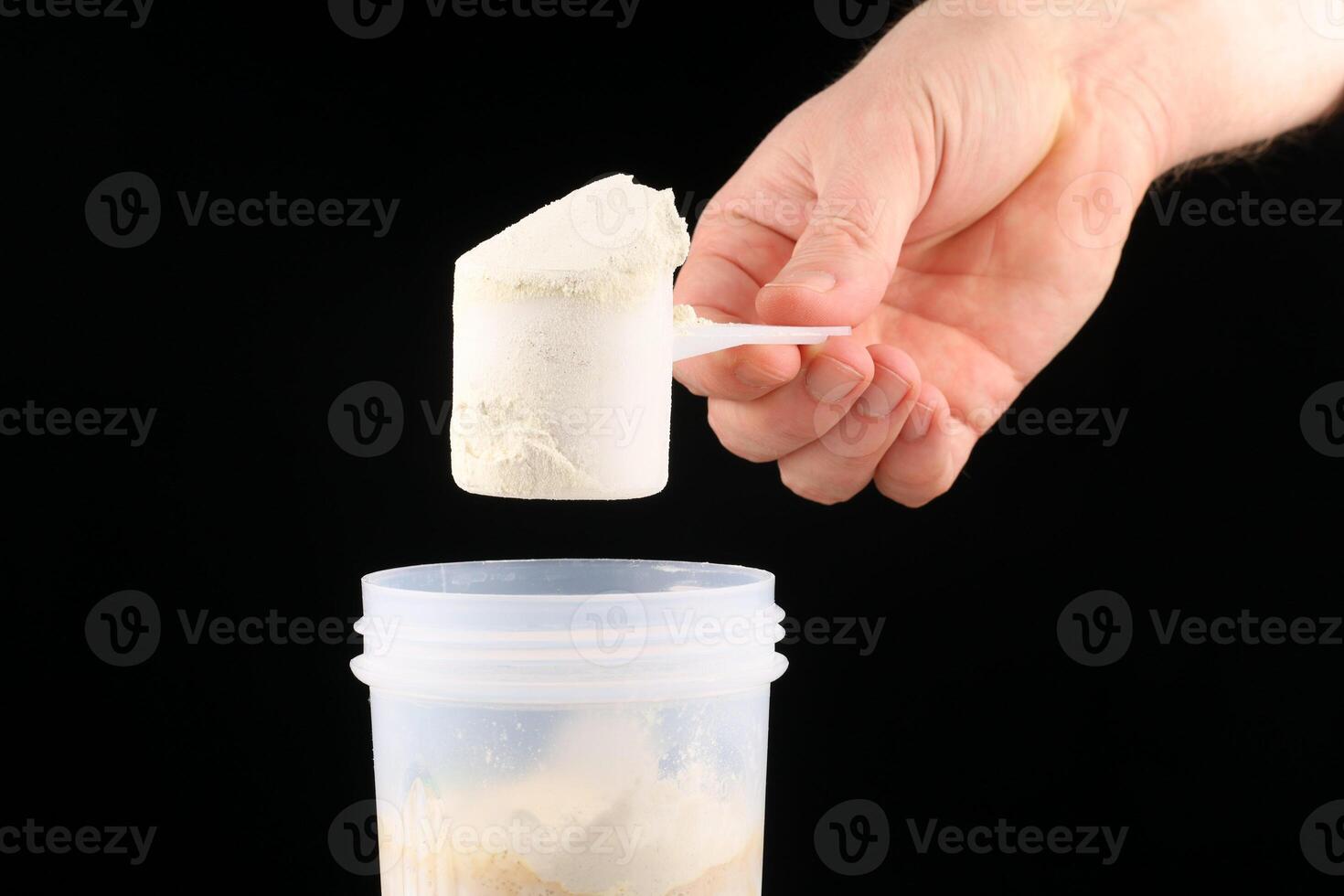A hand holds a scoop of protein near a shaker photo