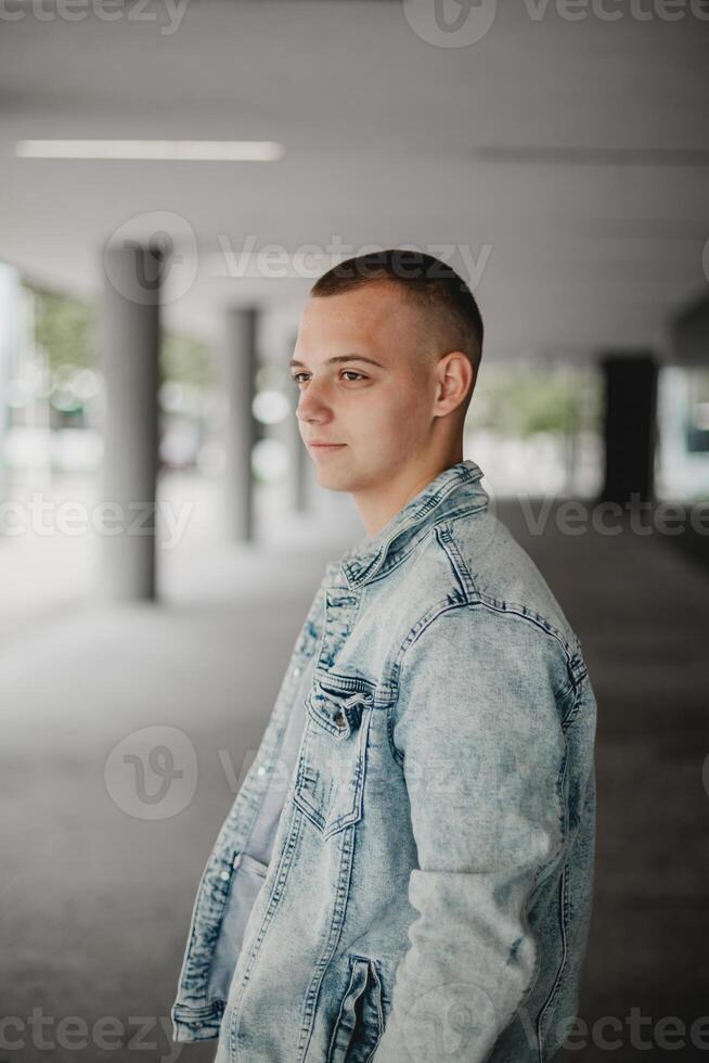 A young man in a blue denim jacket stands in a hallway photo