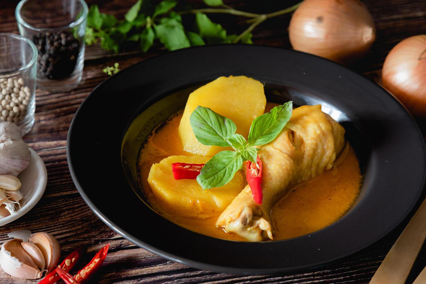 Traditional Thai yellow curry with drumstick chicken, fresh vegetable and herb in bowl on wooden table, Thai food concept photo