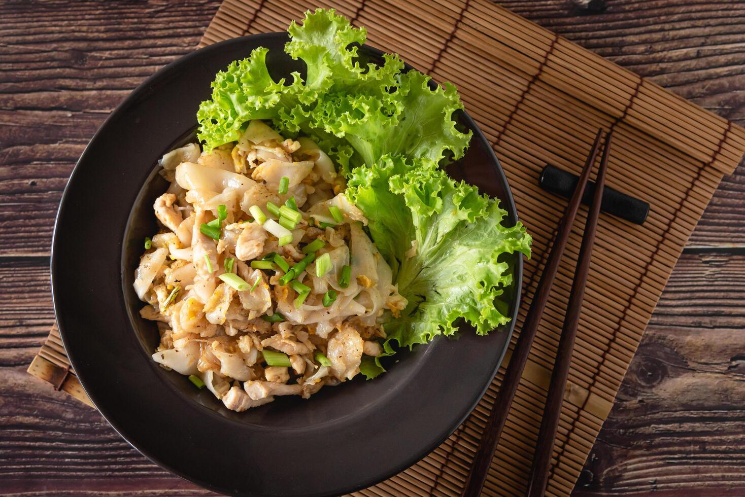 Closed up stir-fried rice noodle with chicken, egg and vegetable on wooden table, Chinese easy cooking photo