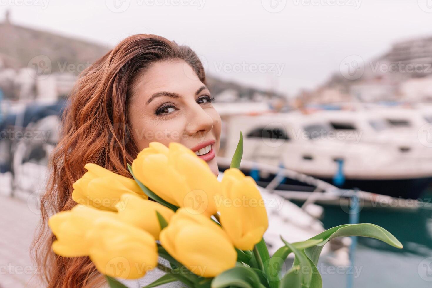 mujer sostiene amarillo tulipanes en puerto con barcos atracado en el fondo., nublado día, amarillo suéter, montañas foto