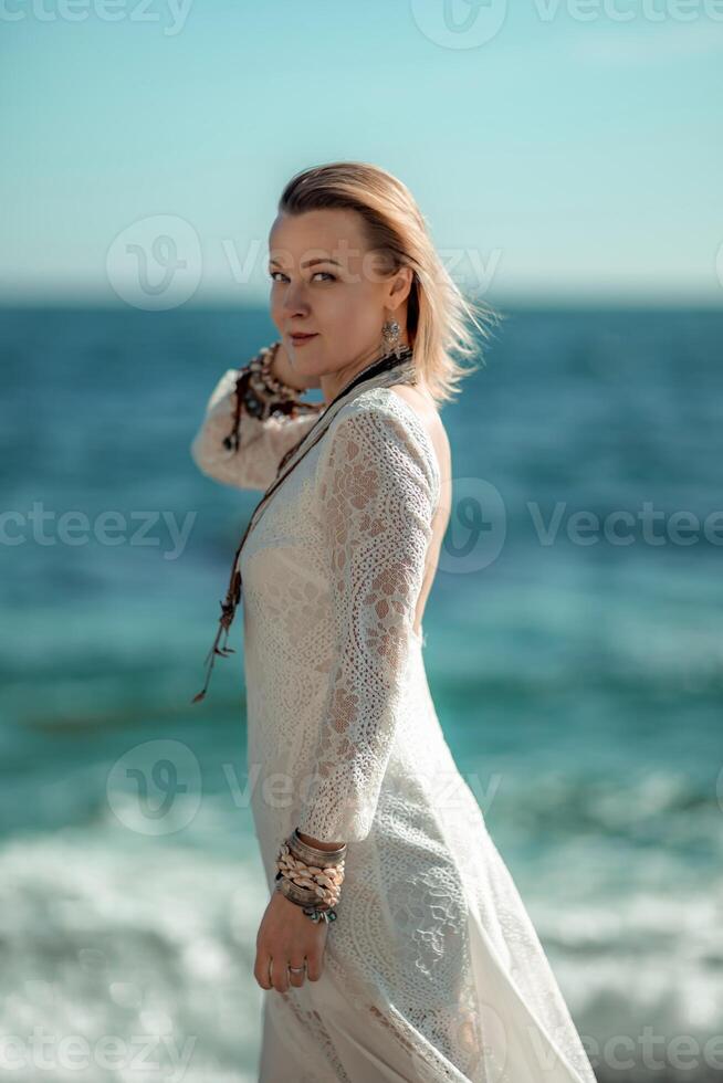 mujer playa mar blanco vestido. el de edad mediana mira bueno con rubia cabello, boho estilo en un blanco largo vestir con playa decoraciones en el cuello y brazos. foto