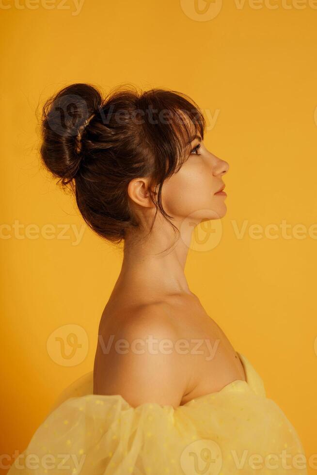 Profile portrait of a beautiful middle-aged woman in a yellow dress, her hair pulled up against a yellow background photo